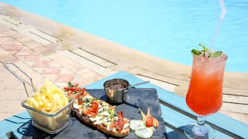 En måltid bestående av en smörgås, pommes frites och en dryck, som serveras på ett bord vid en pool.