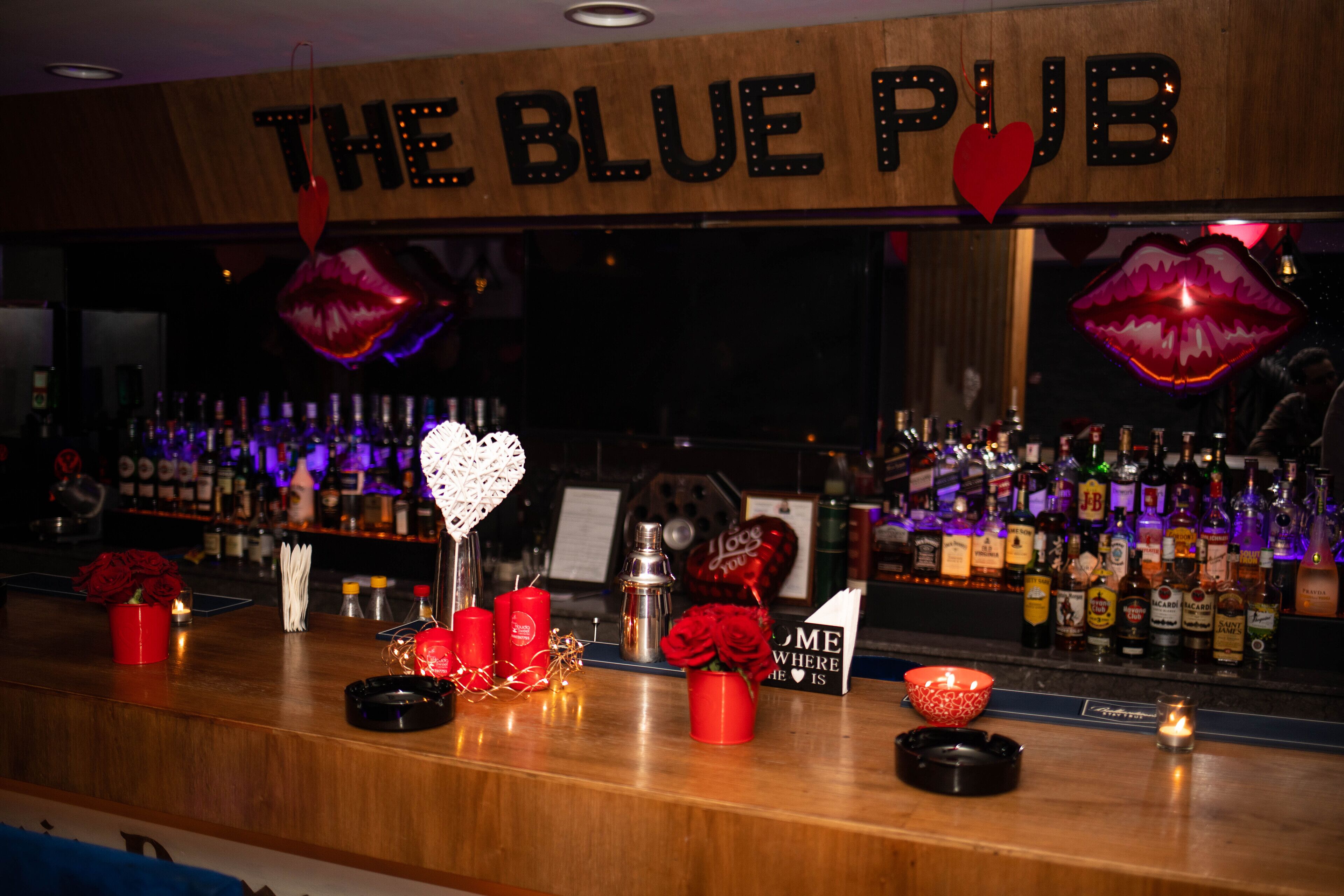 A bar area with a sign reading "The Blue Pub," featuring decorative elements like red roses, candles, and heart-shaped signs.