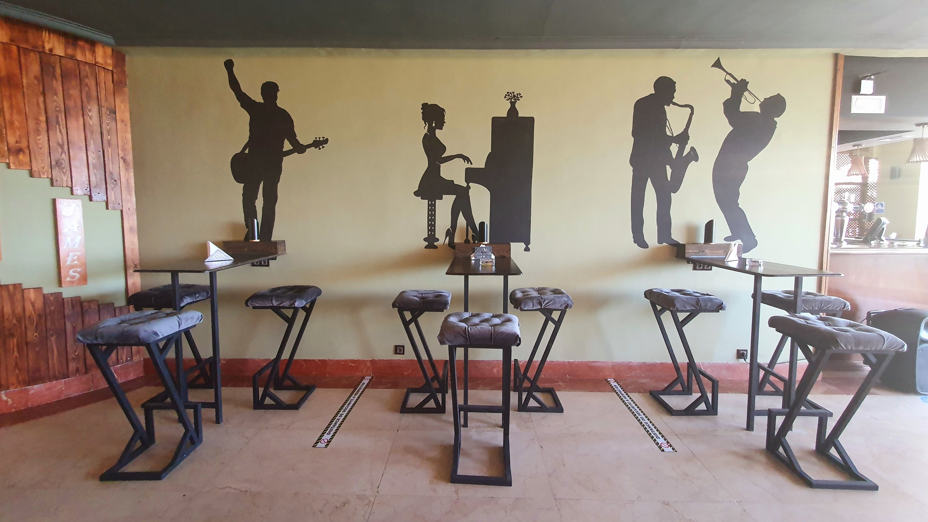 Une pièce avec un mur recouvert de panneaux de bois, une petite table sur laquelle se trouve un ordinateur portable et quatre tabourets.