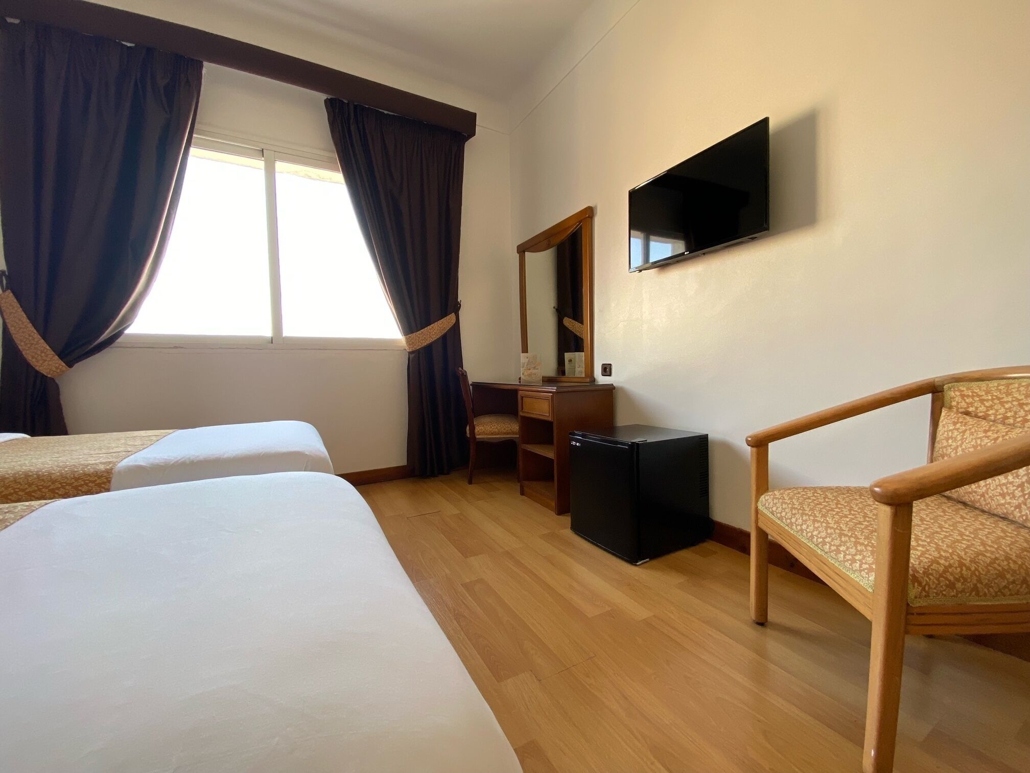 A hotel room with two beds, a desk, a chair, a television, and a window with curtains.