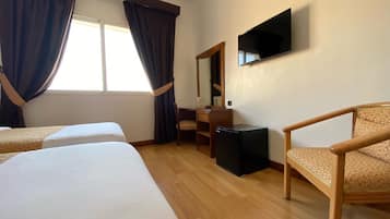 A hotel room with two beds, a desk, a chair, a television, and a window with curtains.