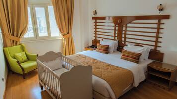 A bedroom with a crib, a green armchair, a wooden headboard, and a bedside table.