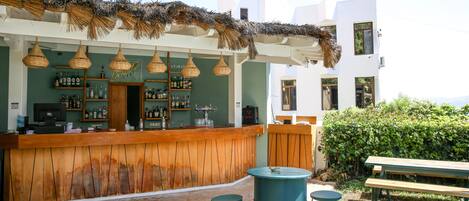 A bar area with a wooden counter, hanging wicker lights, and a thatched roof.