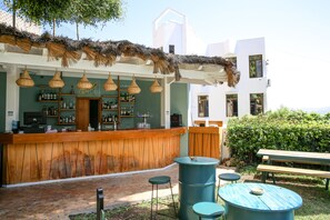 A bar area with a wooden counter, hanging wicker lights, and a thatched roof.