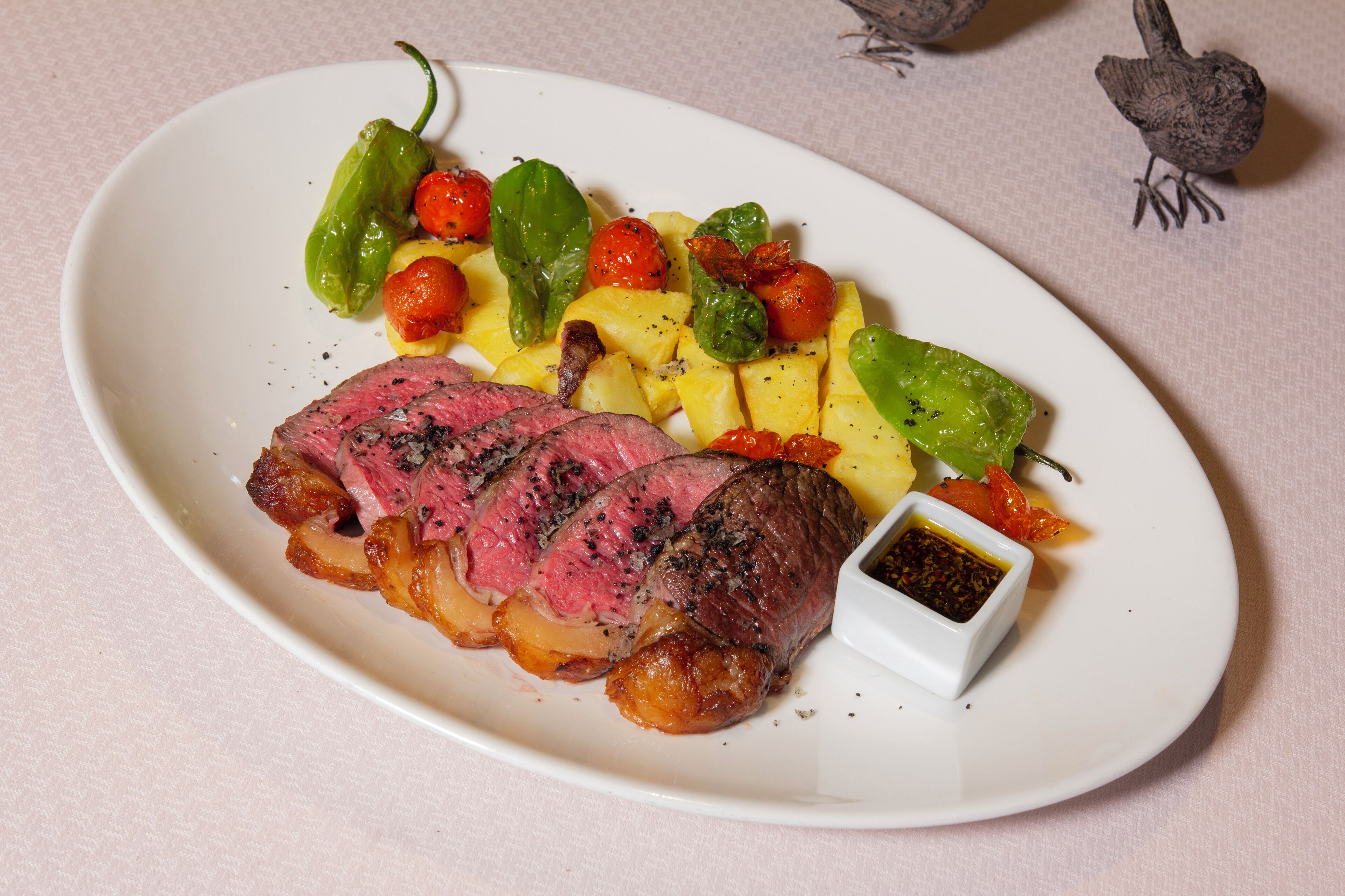 A plate of steak with vegetables and a small dish of sauce.