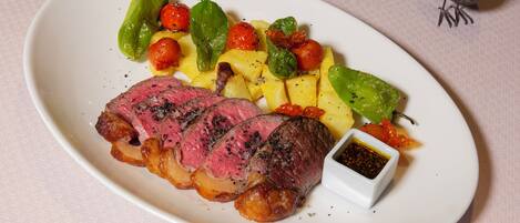 A plate of steak with vegetables and a small dish of sauce.