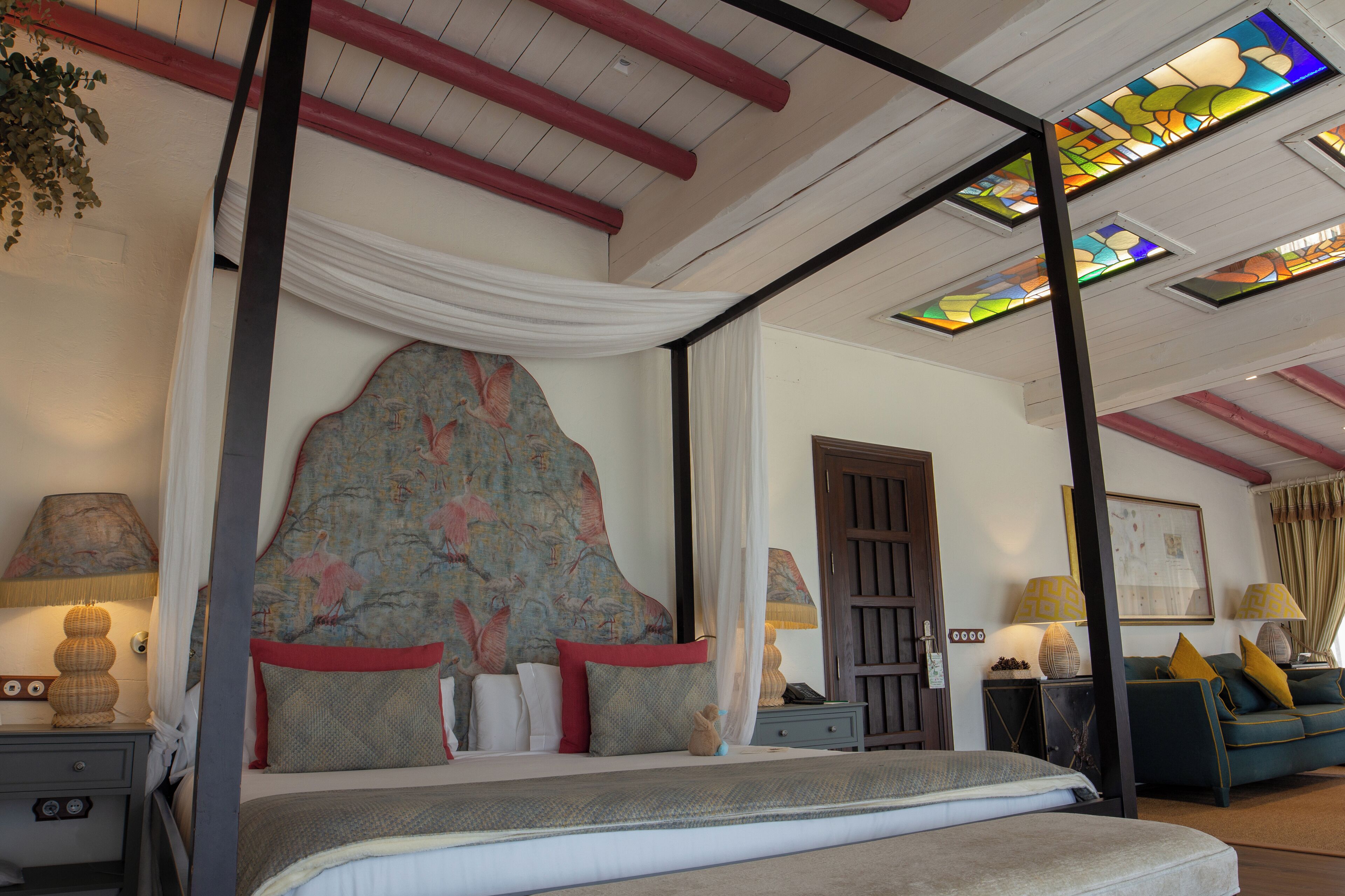 Una camera da letto con un letto a baldacchino, un comodino, un divano e un soffitto decorato con vetrate colorate.