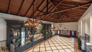 A spacious lobby with a high wooden ceiling, a checkered floor, and a long display of potted plants and decorative items.