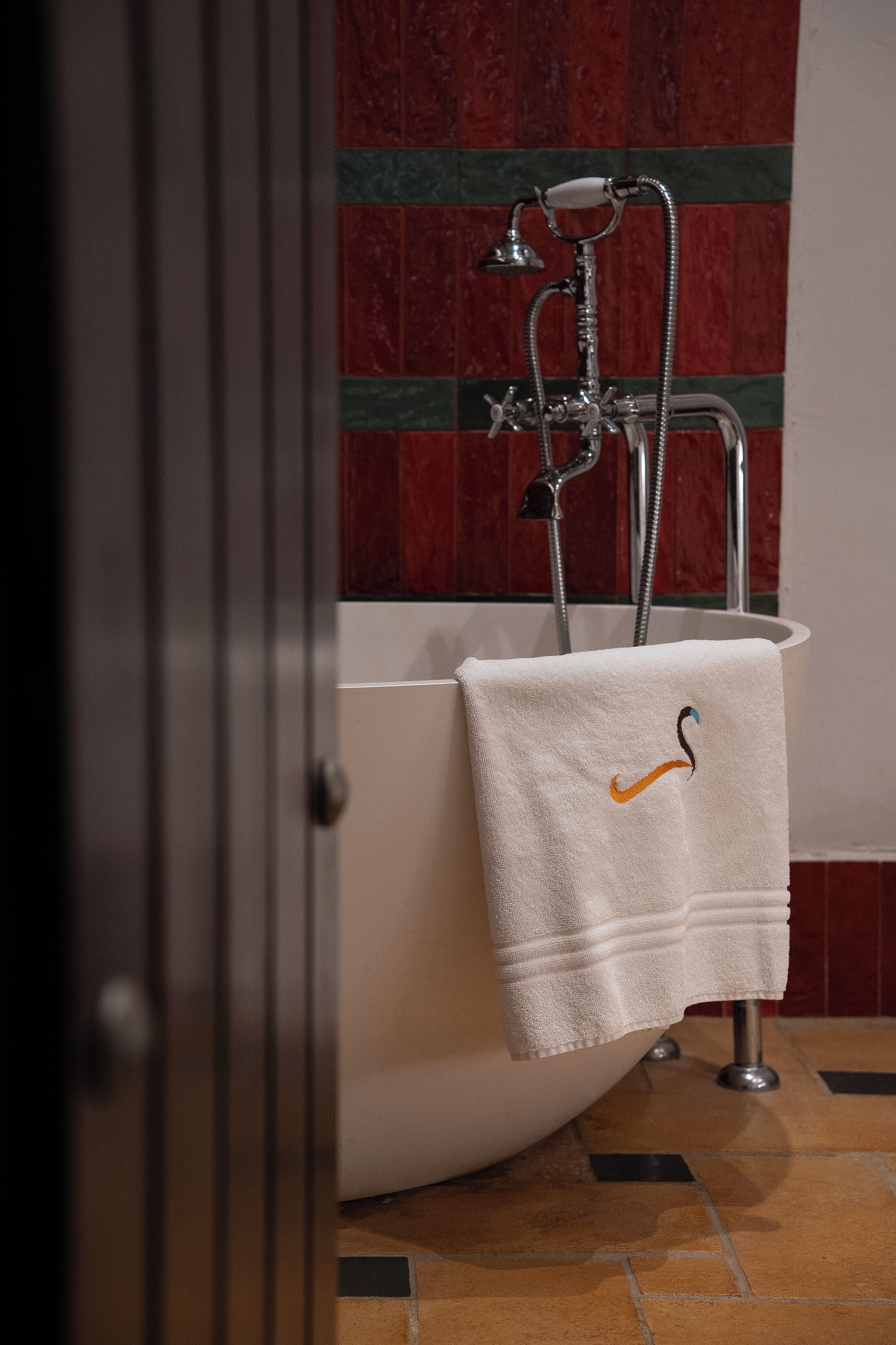Un baño con una bañera blanca, una toalla con un gancho y una ducha con accesorios cromados.