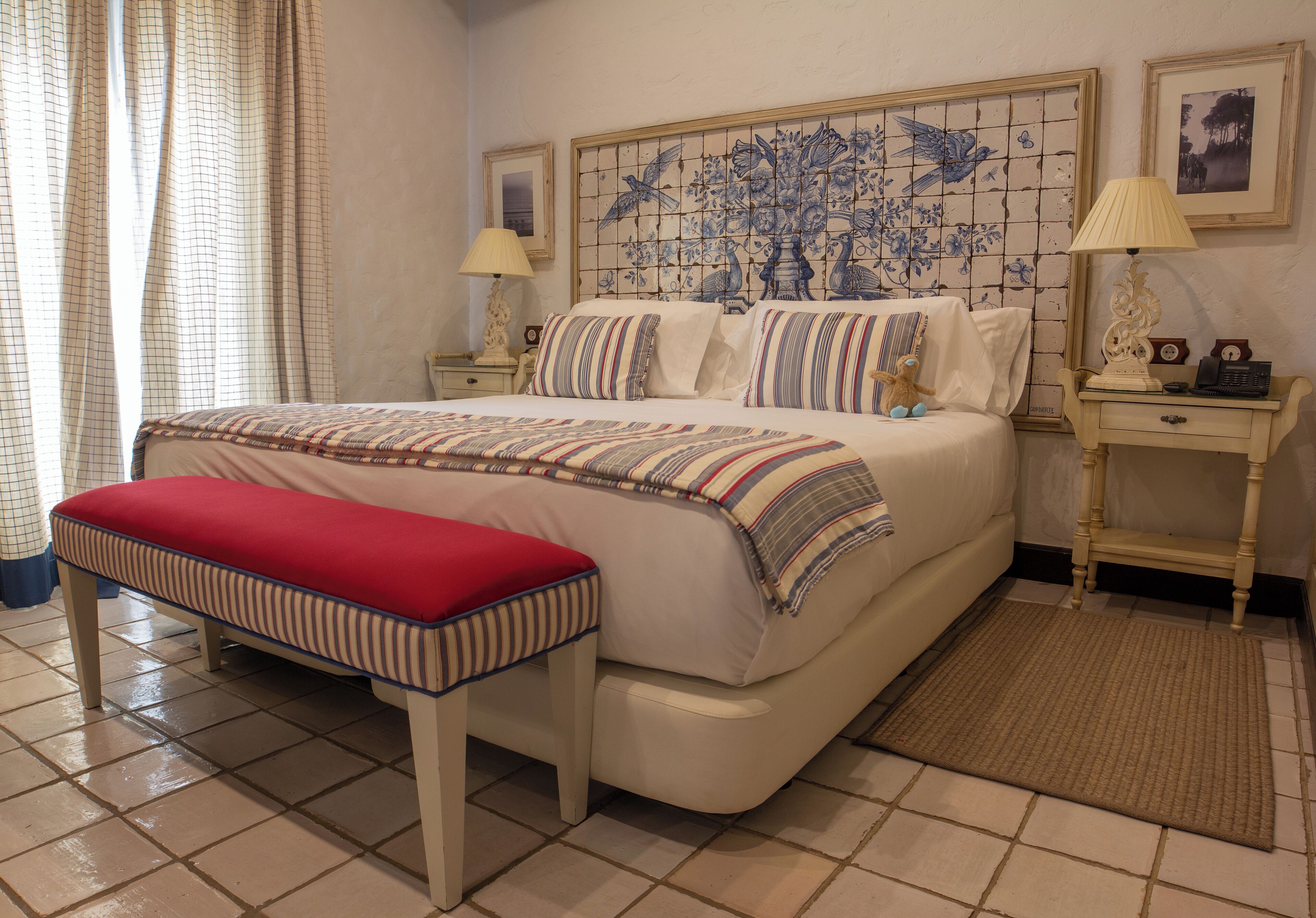 Une chambre à coucher comprenant un lit, un banc, une table de chevet et un mur orné d’un motif décoratif en carreaux.