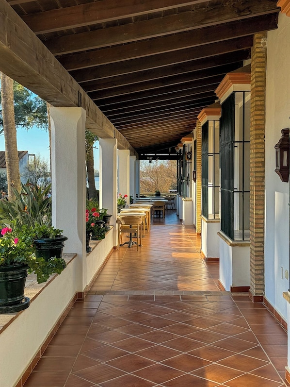 A covered patio with tiled flooring, outdoor seating, and potted plants.