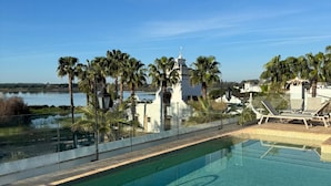 A clear blue sky, a swimming pool with lounge chairs, palm trees, and a view of a body of water. - Hotel La Malvasía by Kaizen Hoteles (Almonte)
