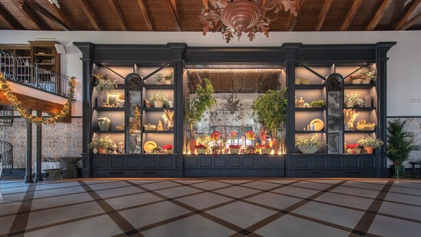 A lobby with a checkered floor, a staircase, and a wall with shelves displaying various items. - Hotel La Malvasía by Kaizen Hoteles (Almonte)
