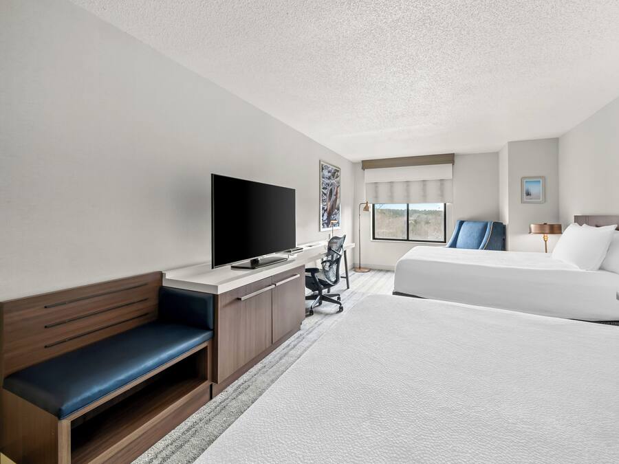 A hotel room with a large bed, a desk with a flat-screen TV, a chair, and a window with a view.