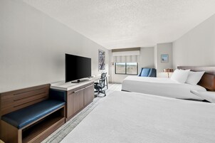 Habitación de hotel con una cama grande, un escritorio, un televisor de pantalla plana, una silla y una ventana con vistas.