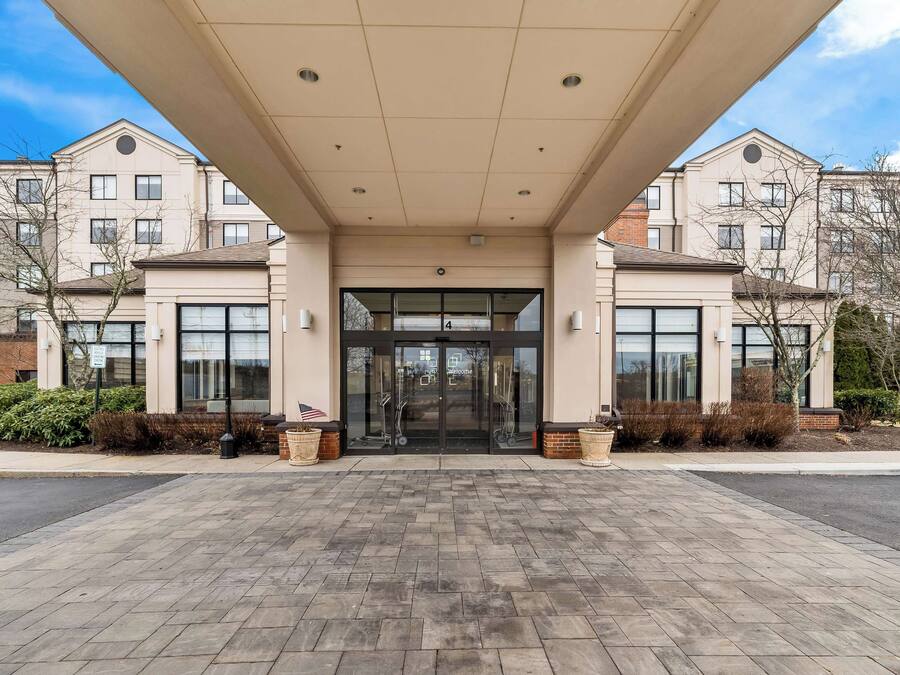 A modern building entrance with a covered walkway, large windows, and a welcoming sign.