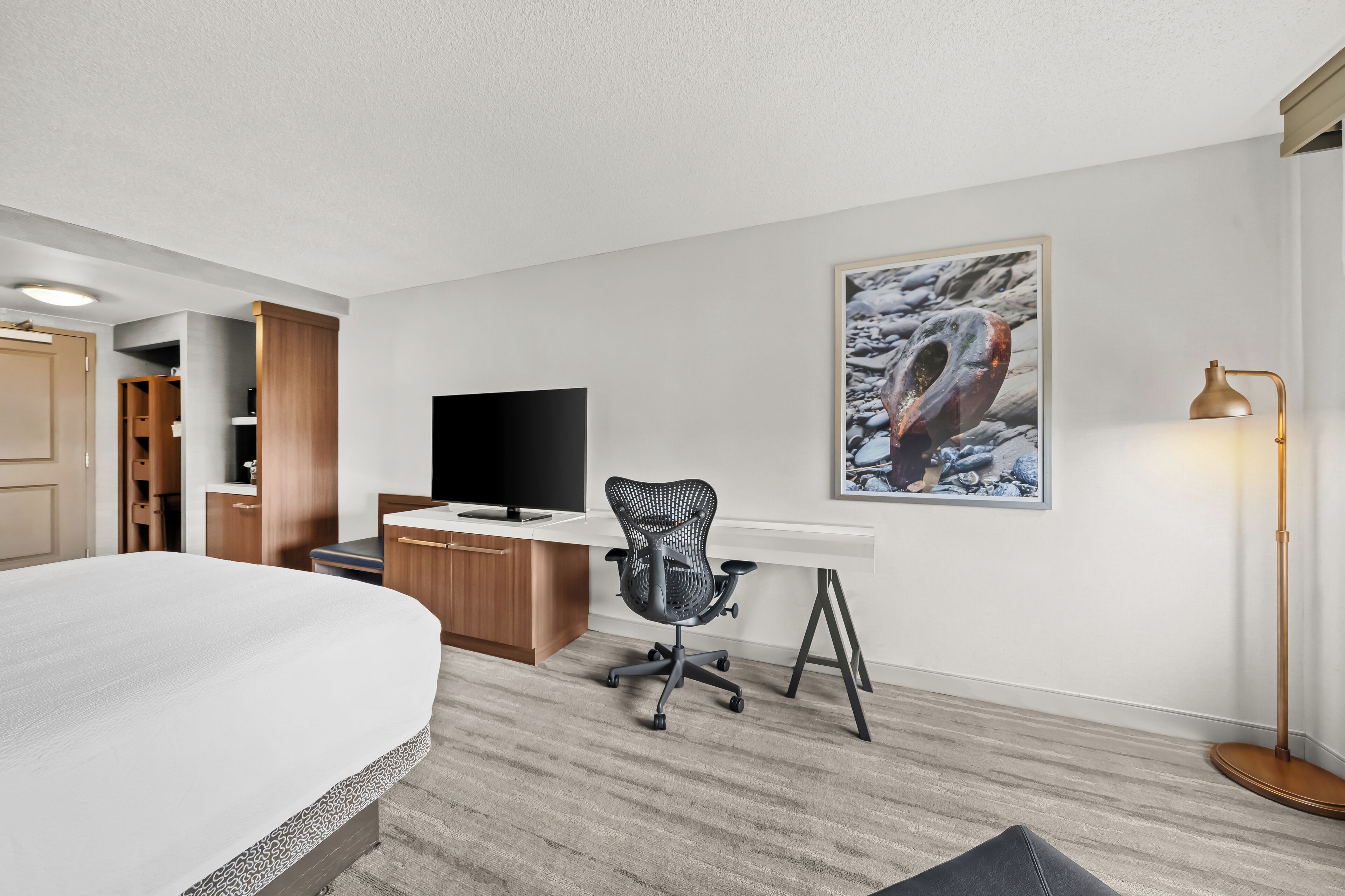 Ein Hotelzimmer mit Bett, Schreibtisch, Stuhl, Fernseher und einem Bild an der Wand.