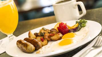 En morgenmadstallerken med æg, kartofler og pølse, samt et glas appelsinjuice og en kaffekop.