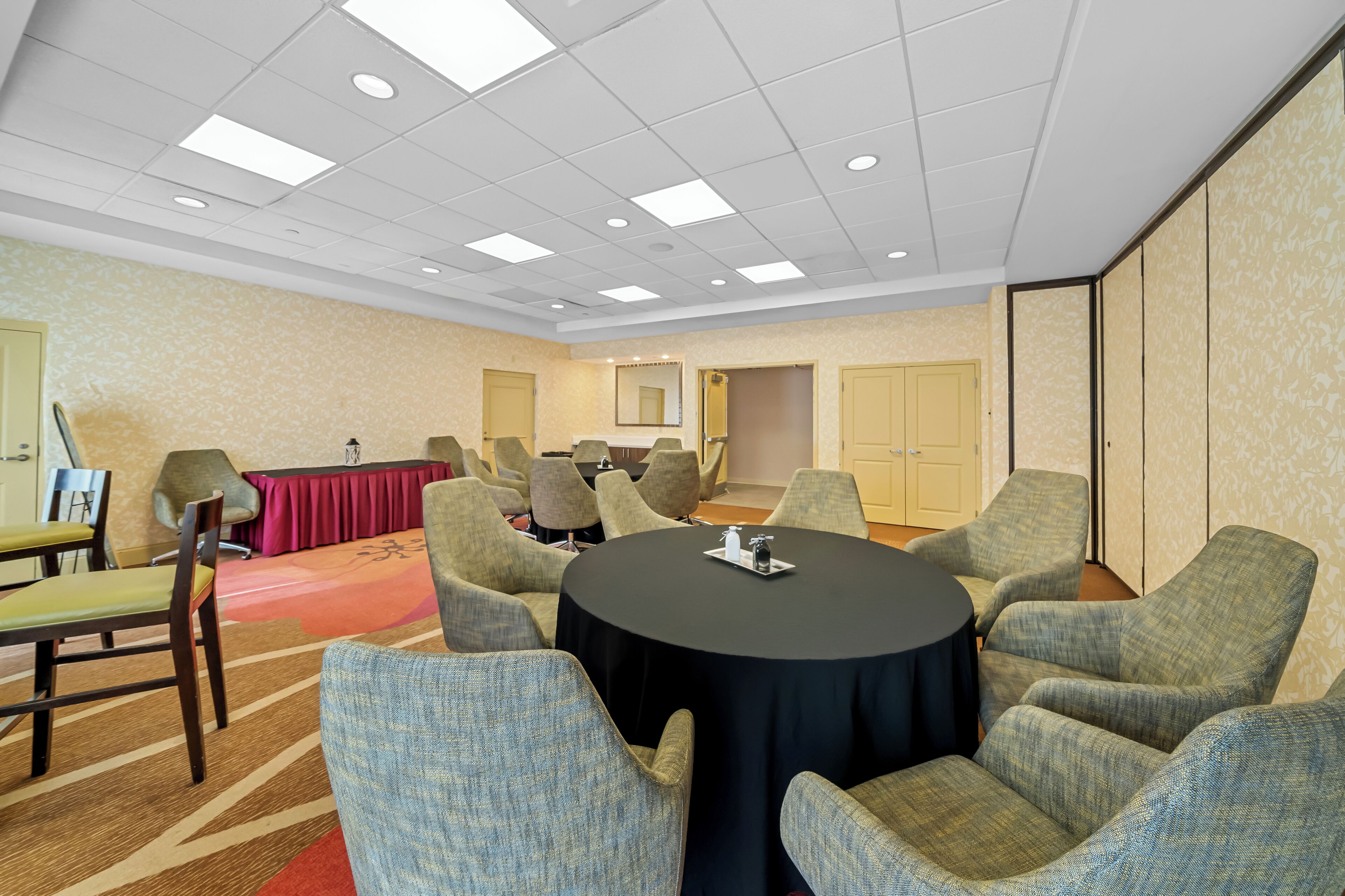 A conference room with a round table, multiple chairs, a red carpet, and a patterned wall.