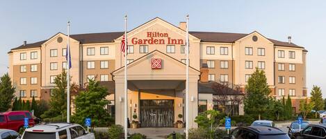 A Hilton Garden Inn with a central entrance, parking lot, and surrounding greenery.