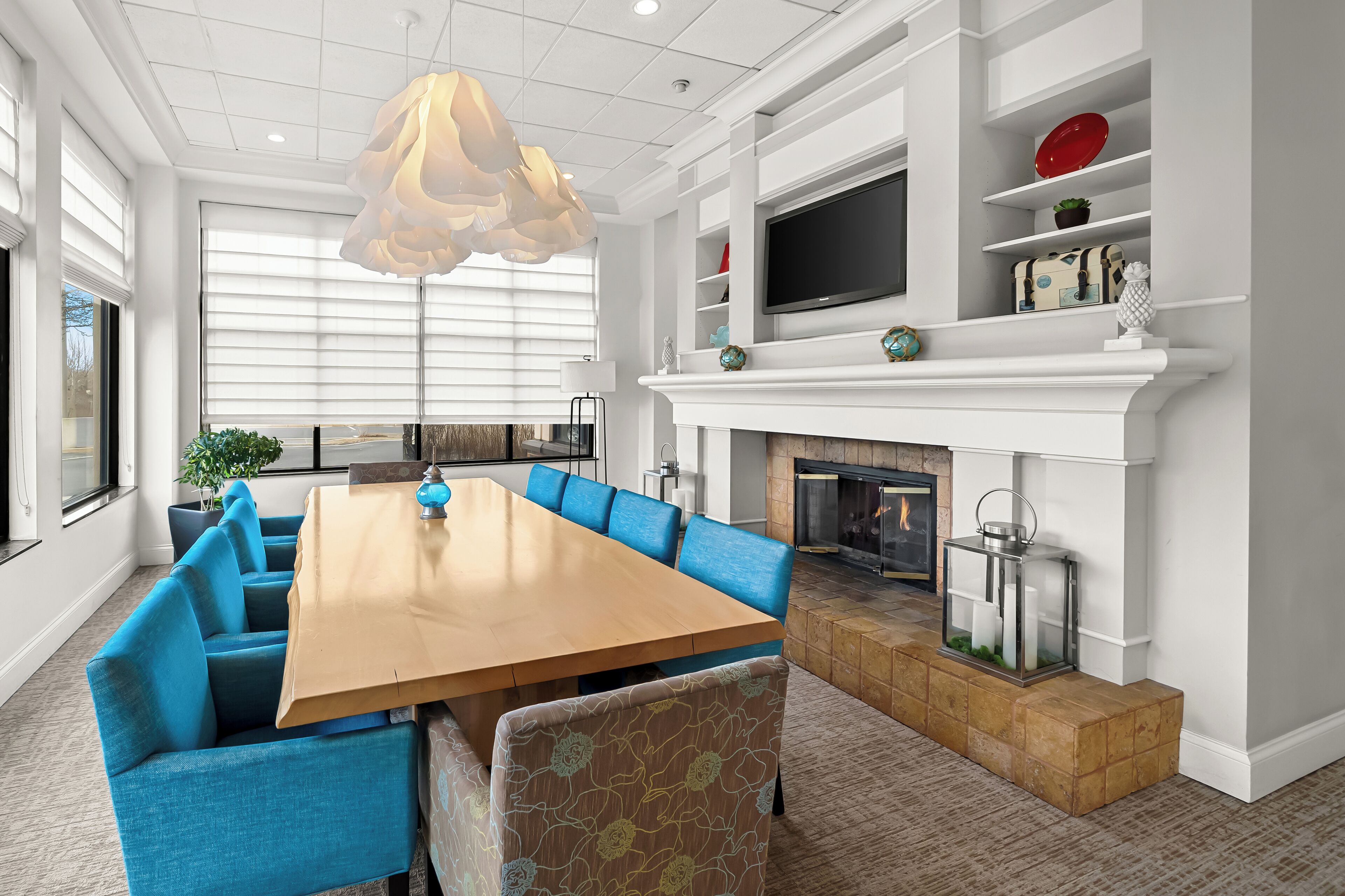 A modern living room with a large wooden dining table, blue upholstered sofas, a fireplace, and a mounted TV.