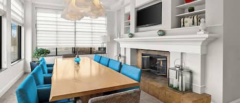 Una sala de estar moderna con una gran mesa de comedor de madera, sofás tapizados en azul, una chimenea y un televisor montado en la pared.