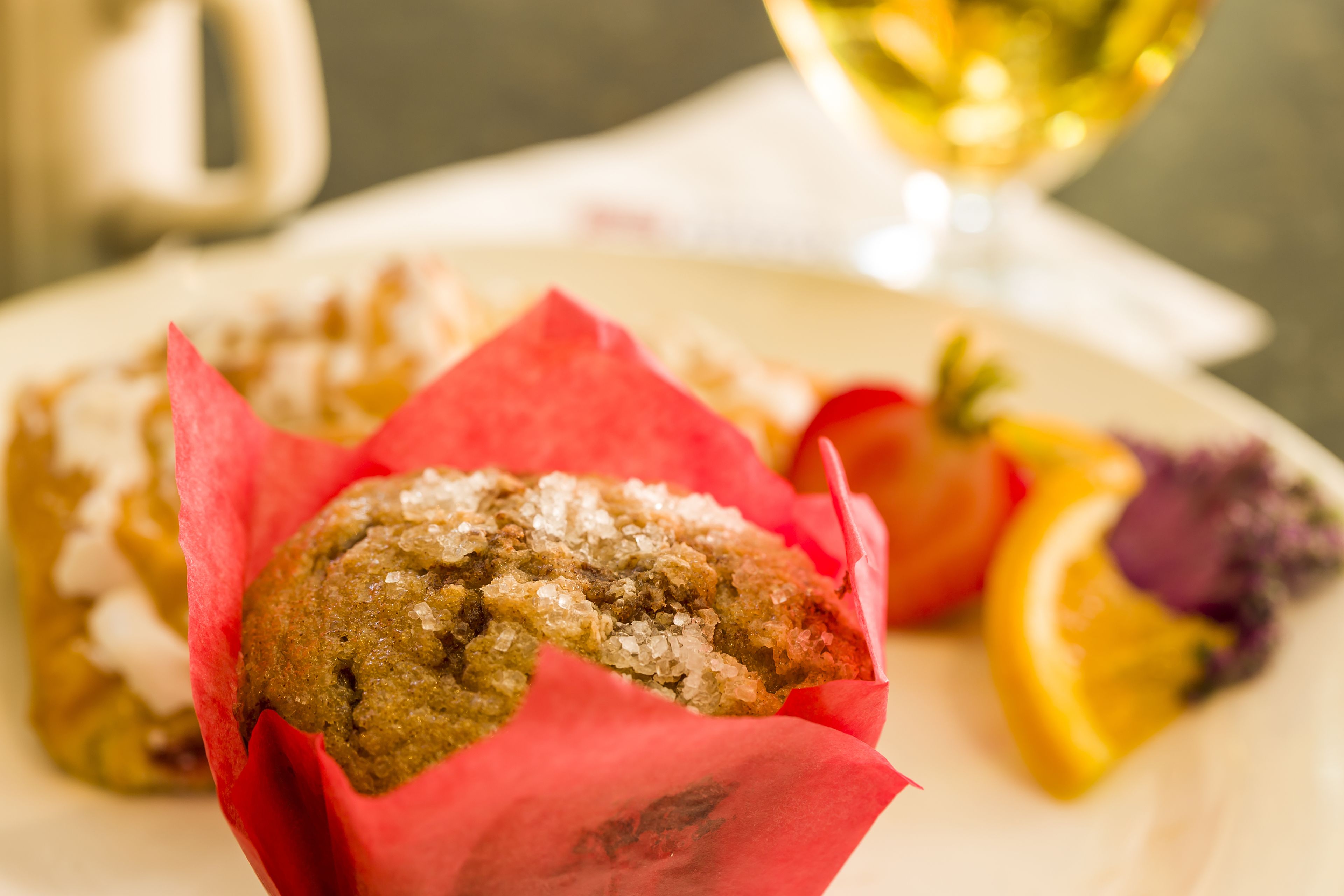 Un muffin en un envoltorio rojo con una rodaja de naranja y un vegetal morado sobre un plato.