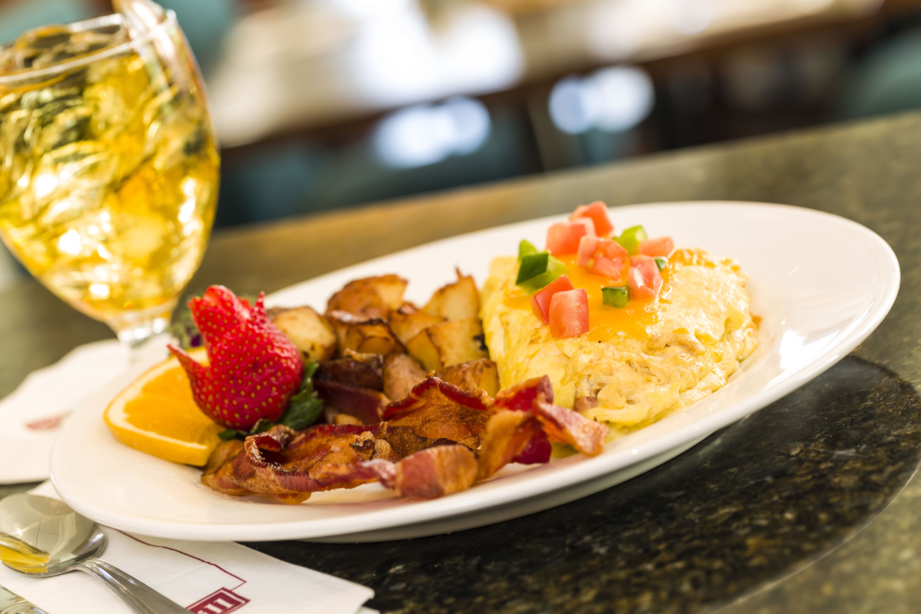 A breakfast plate with eggs, bacon, and fruit on a white plate.