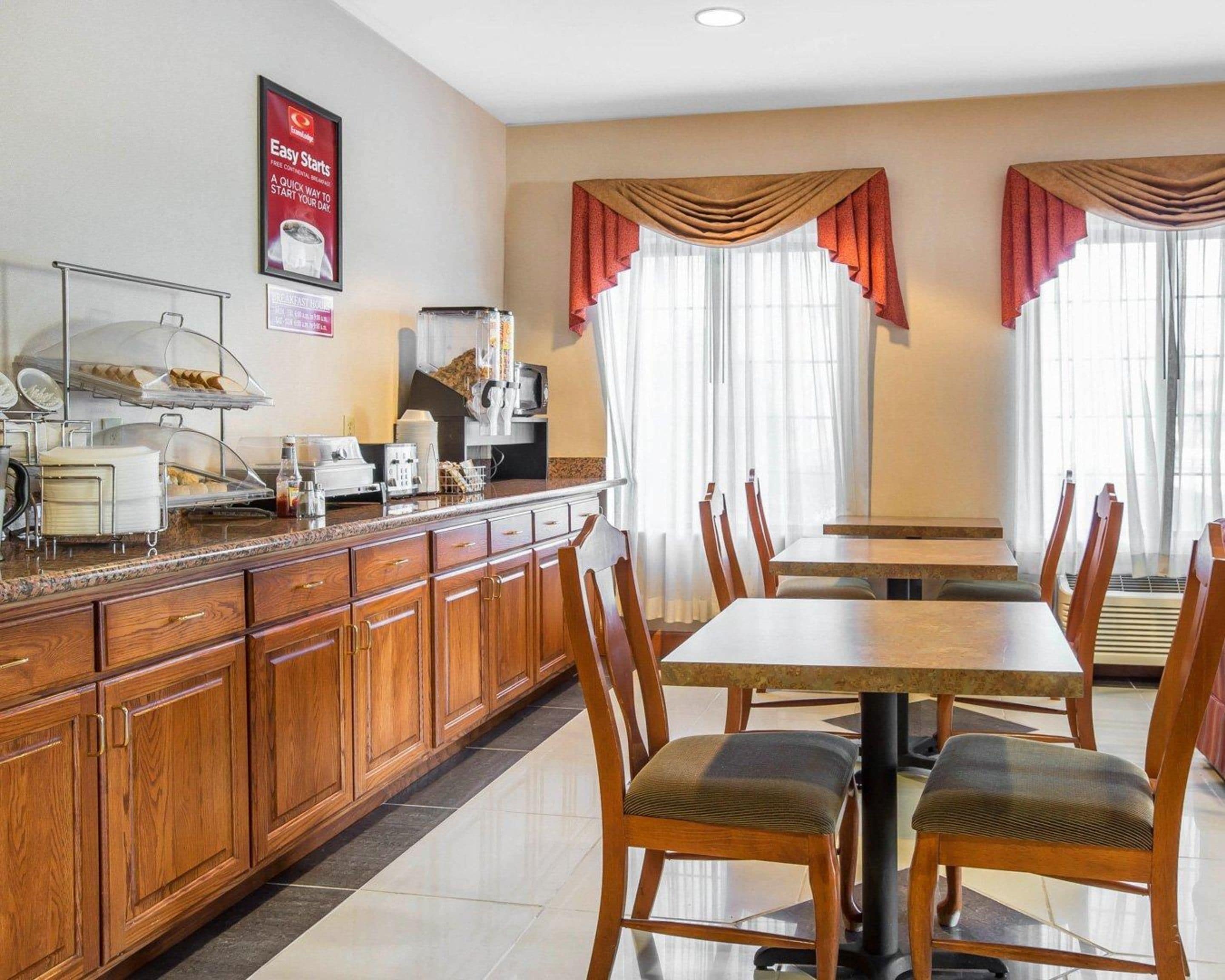 A hotel dining area with wooden cabinets, a buffet setup, and a large window with curtains.