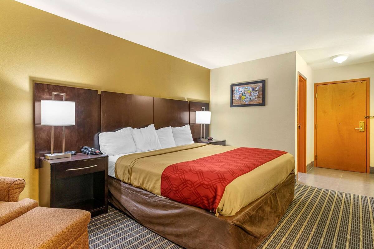 A hotel room with a bed, two bedside tables, a chair, a door, and a wall-mounted artwork.