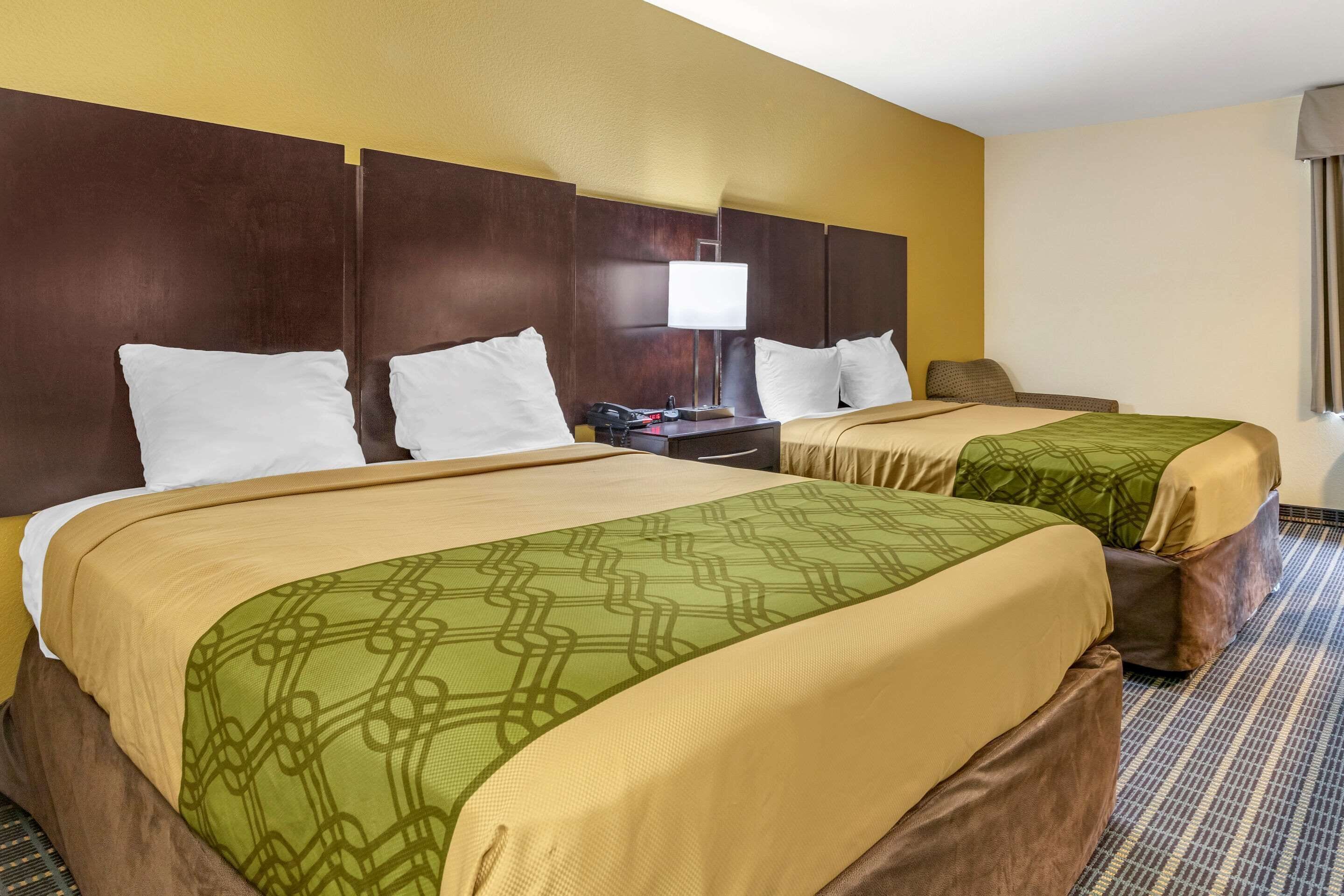 A hotel room with two beds, a nightstand, and a lamp.