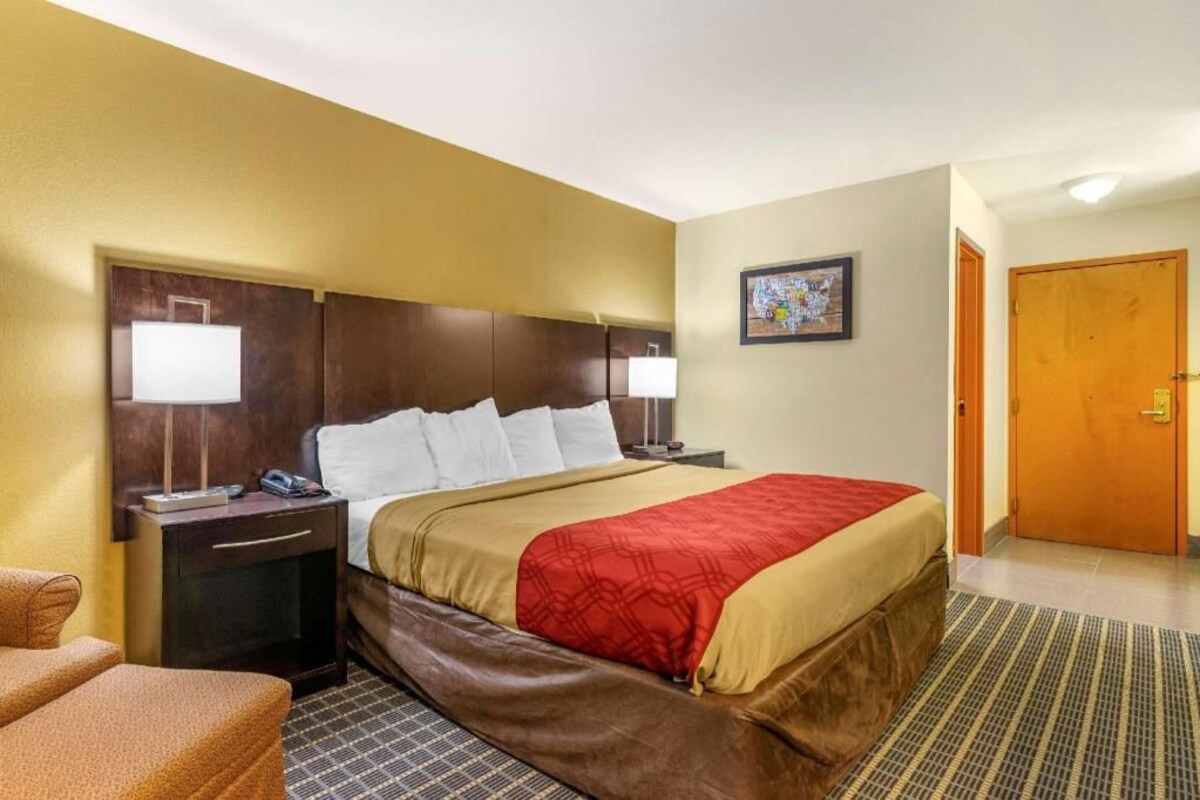 A hotel room with a bed, two bedside tables, a lamp, a chair, and a door.