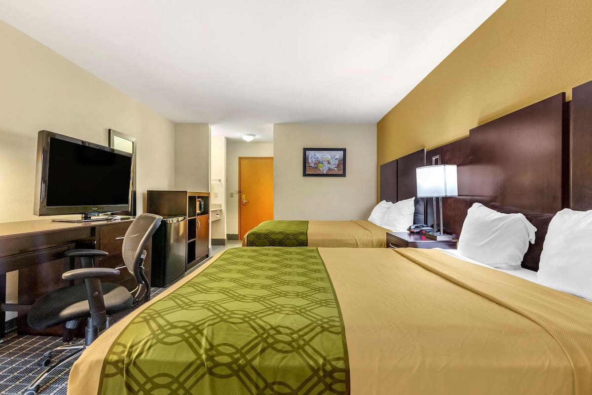 A hotel room with a bed, a desk with a TV, a chair, and a lamp.