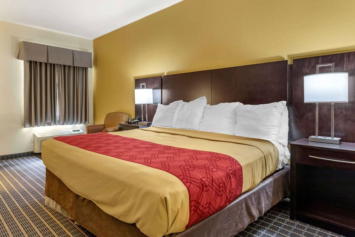 A hotel room with a large bed, a desk, a chair, a lamp, and a window with curtains.