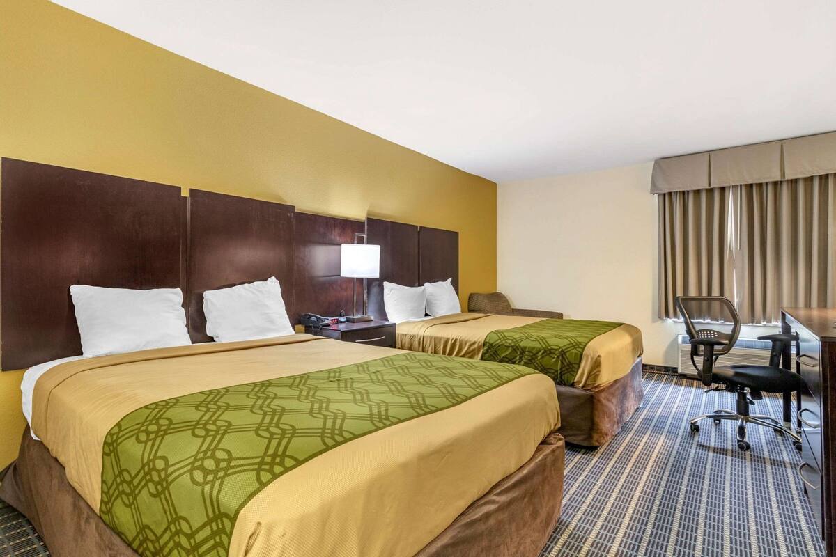 A hotel room with two beds, a desk, a chair, and a window with curtains.