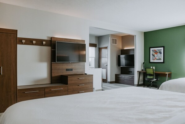 A hotel room with a large bed, a wooden dresser, a flat-screen TV, a desk with a chair, and a green accent wall.