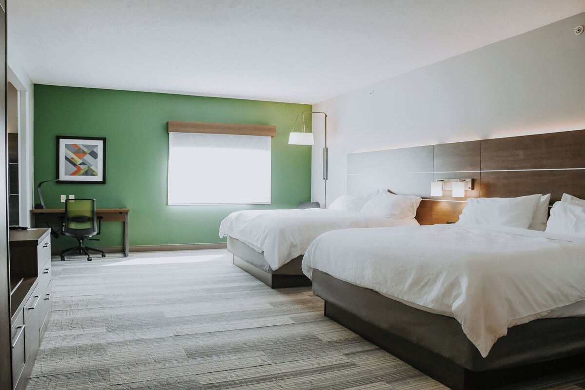 A hotel room with two beds, a desk, and a chair.