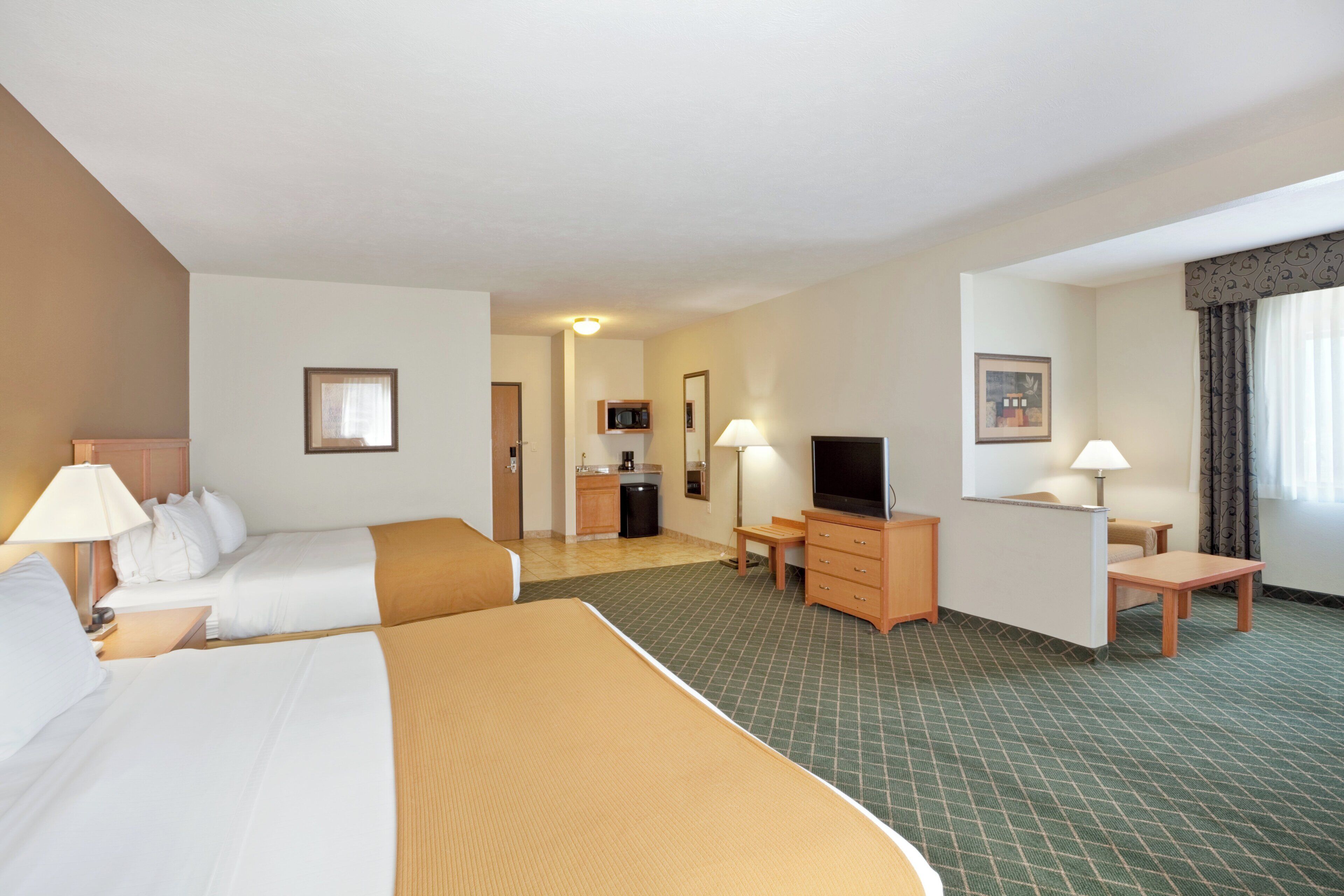 A hotel room with two beds, a desk, a television, and a kitchenette.