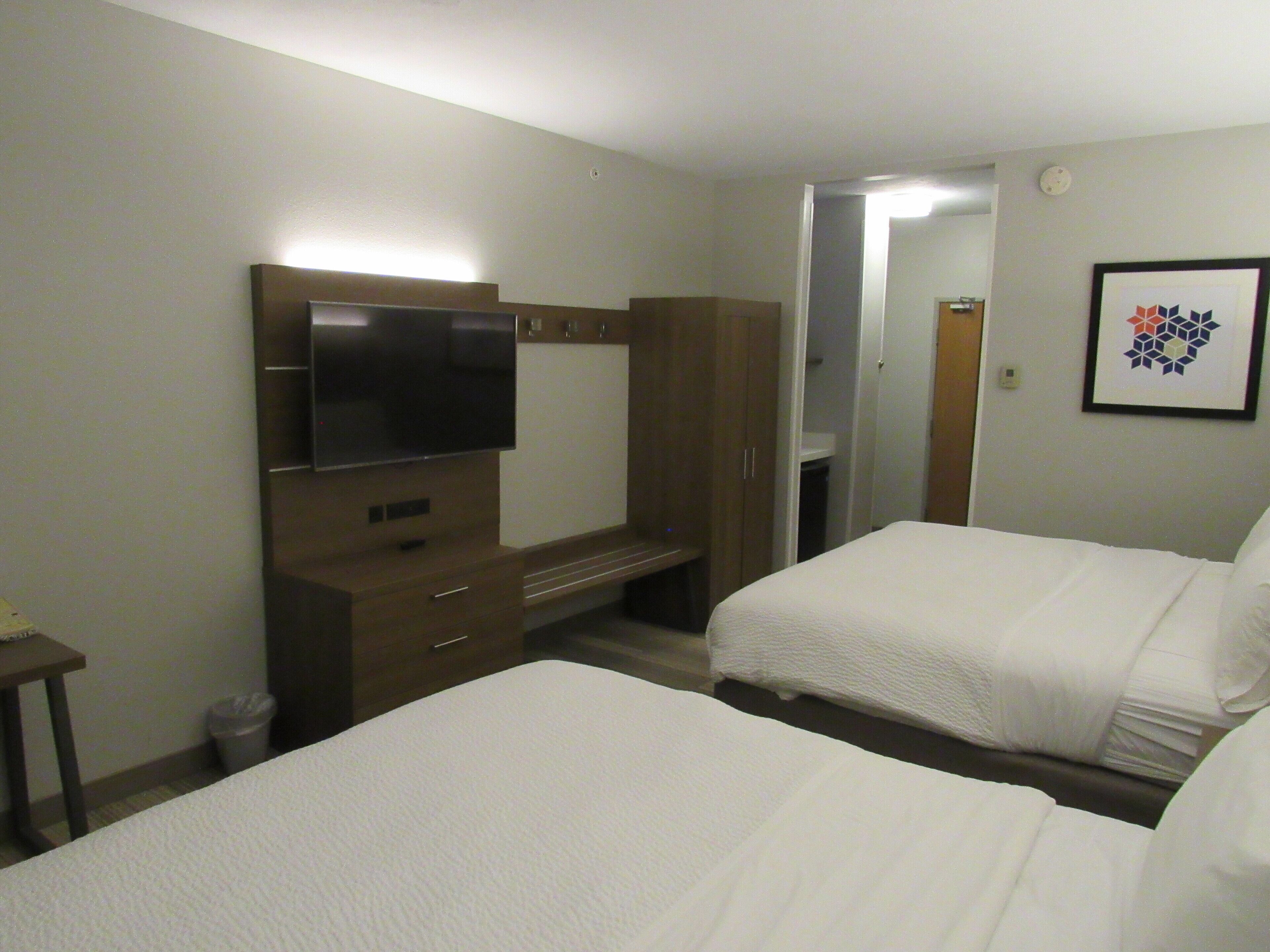 Une chambre d’hôtel avec deux lits, une télévision, une armoire et un tableau encadré au mur.