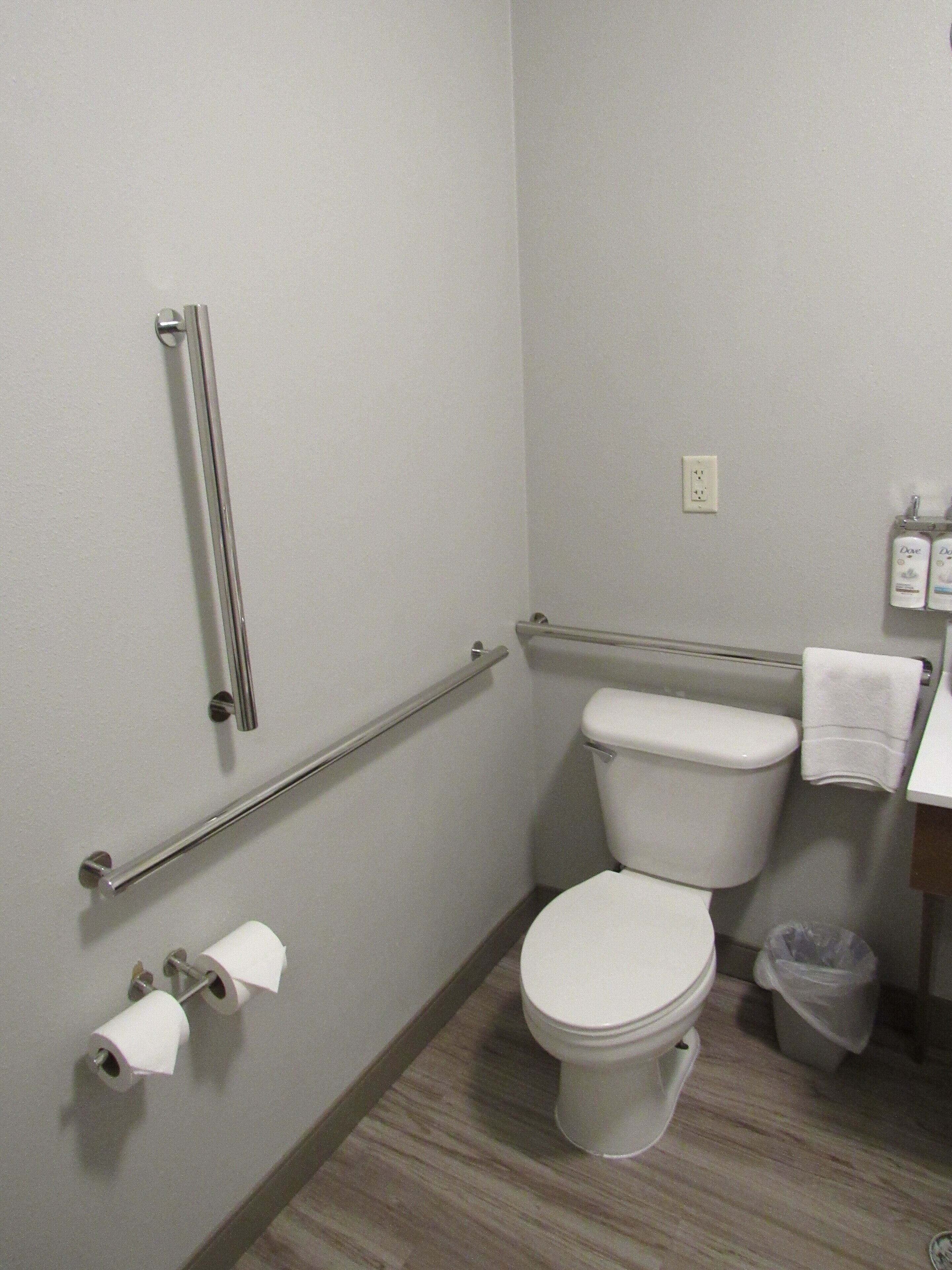 A bathroom with a white toilet, a grab bar, a towel rack, and a trash bin.