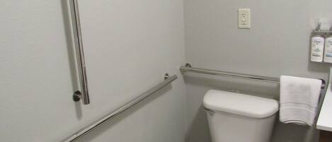 A bathroom with a white toilet, a grab bar, a towel rack, and a trash bin.