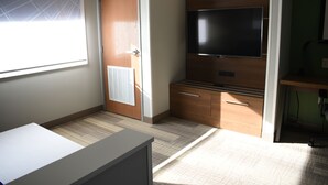 A hotel room with a large window, a flat-screen TV mounted on the wall, a wooden cabinet, and a desk. - Holiday Inn Express & Suites South - Lincoln by IHG (Lincoln)