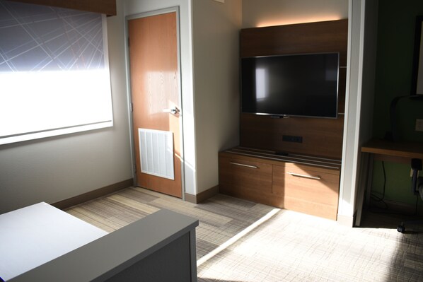 A hotel room with a large window, a flat-screen TV mounted on the wall, a wooden cabinet, and a desk. - Holiday Inn Express & Suites South - Lincoln by IHG (Lincoln)