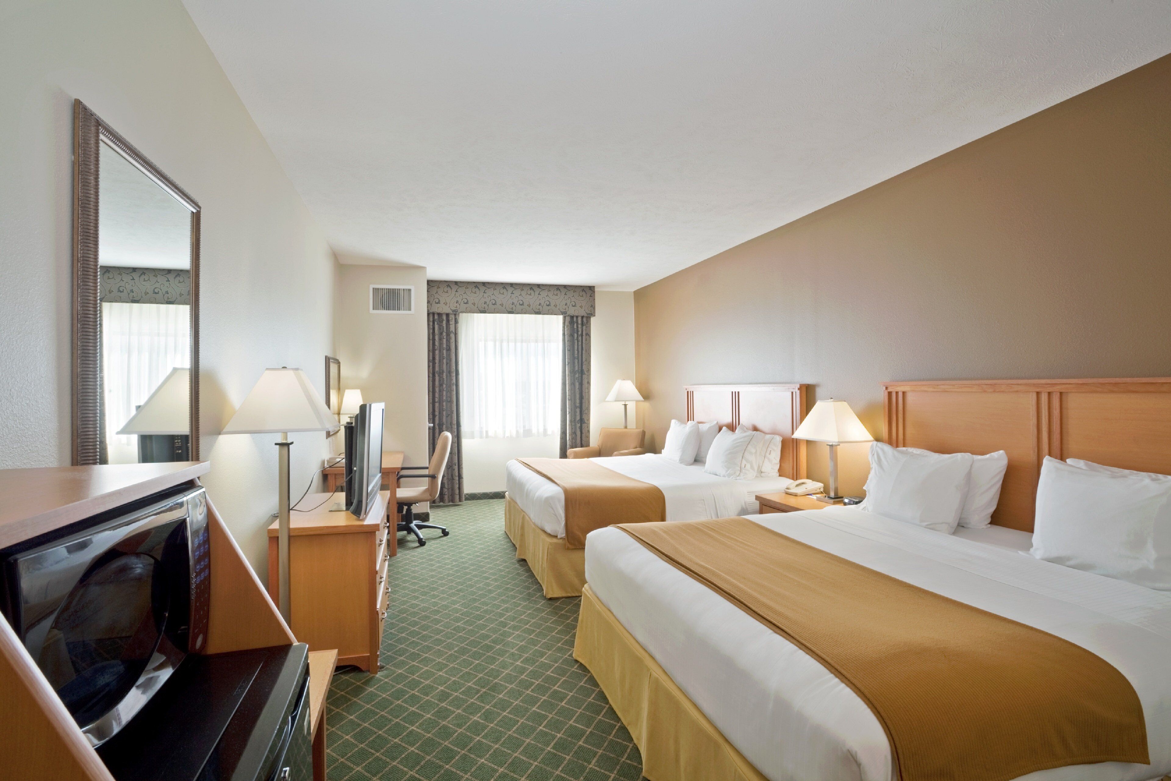 A hotel room with two beds, a desk, a television, and a mirror.
