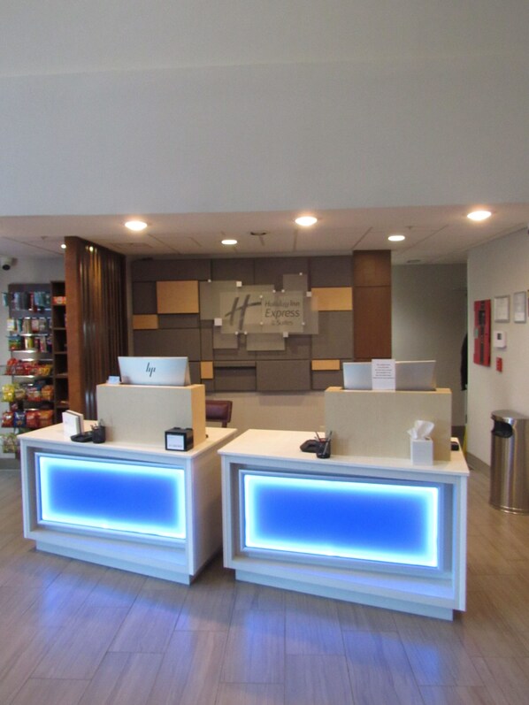 A hotel reception area with two reception desks, a Holiday Inn Express sign, and a small kiosk with snacks. - Holiday Inn Express & Suites South - Lincoln by IHG (Lincoln)
