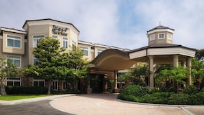A hotel with a large entrance, a covered patio area, and a tower-like structure. - West Inn & Suites (Carlsbad)