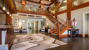 A spacious lobby with a wooden staircase, a reception desk, and a large rug. - West Inn & Suites (Carlsbad)