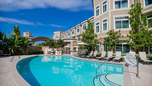 A swimming pool with lounge chairs and a building with multiple windows and balconies. - West Inn & Suites (Carlsbad)
