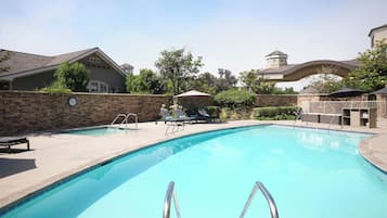 A swimming pool with a stone wall, lounge chairs, and a clock.