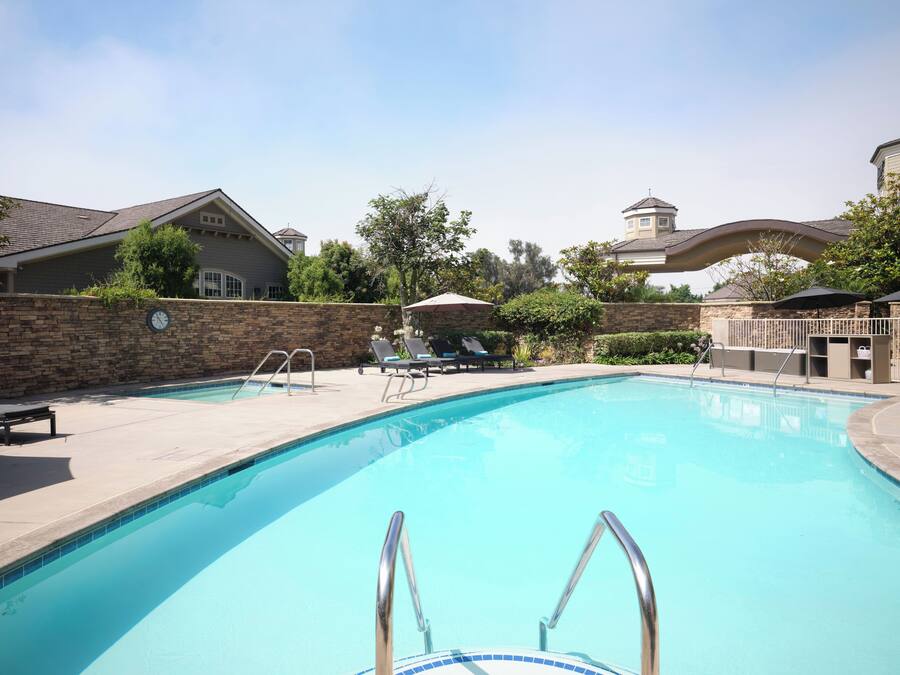 A swimming pool with a stone wall, lounge chairs, and a clock.